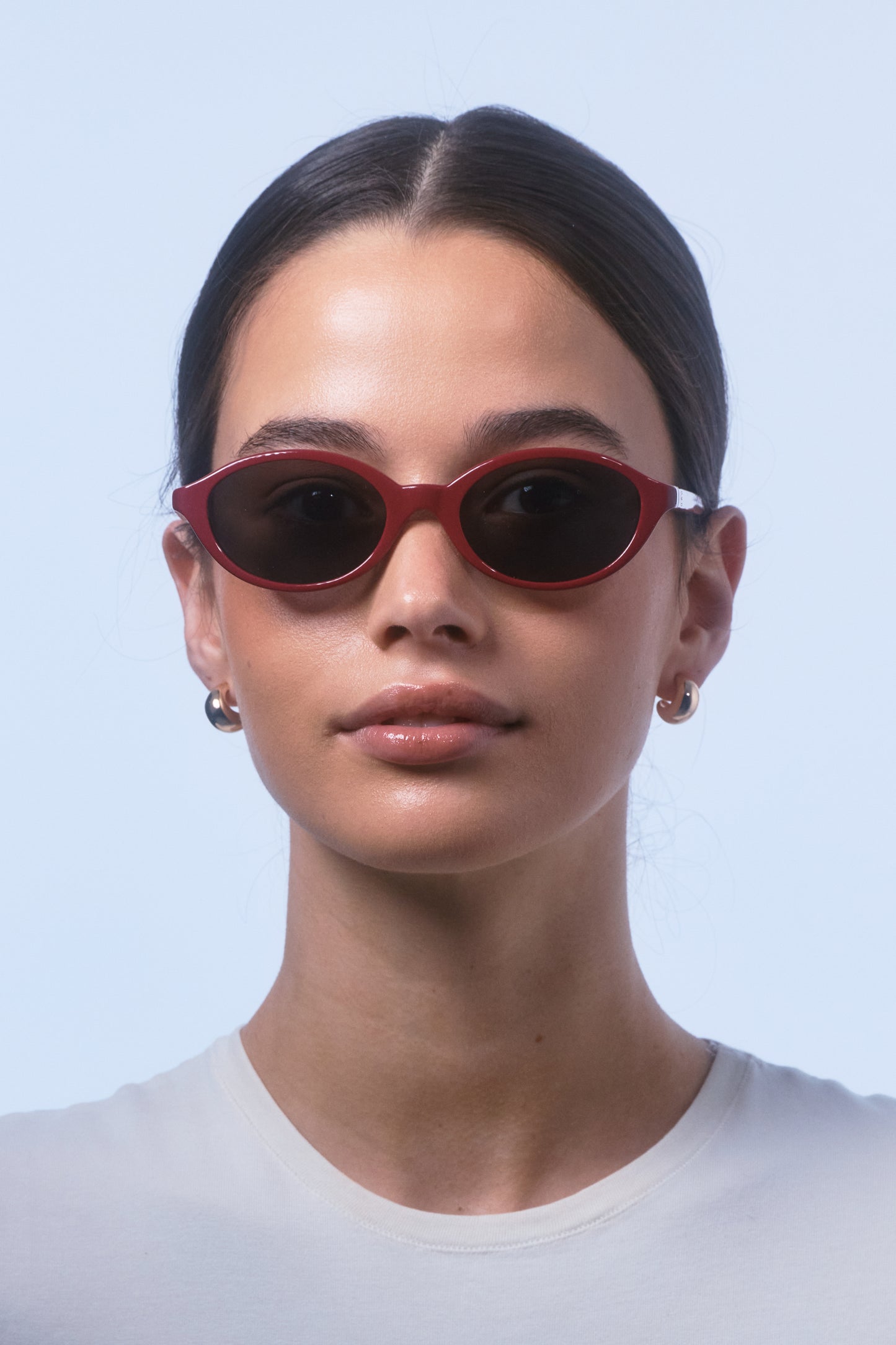 Female model wearing Isle of Eden Mirabel dark red sunglasses, front-facing portrait looking directly at the camera
