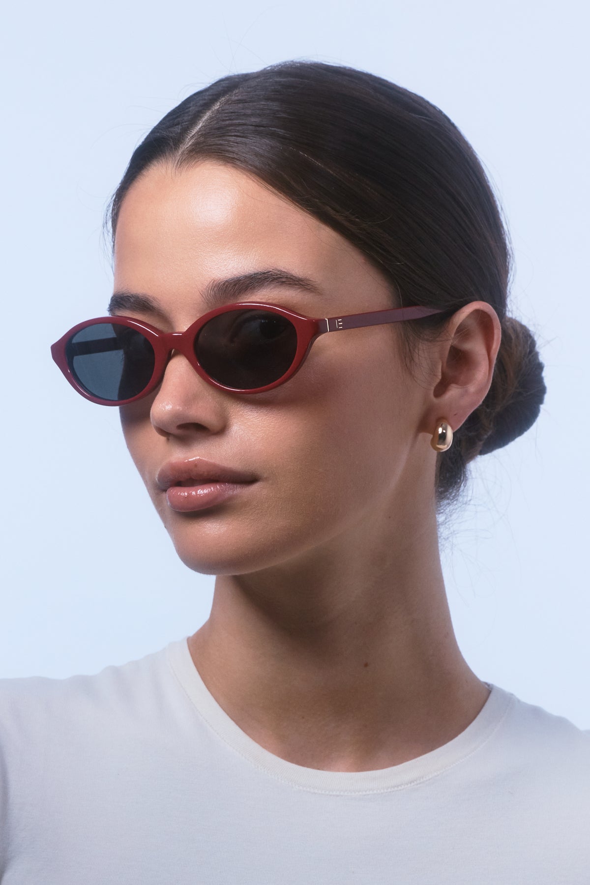 Female model wearing Isle of Eden Mirabel dark red sunglasses, angled portrait looking away