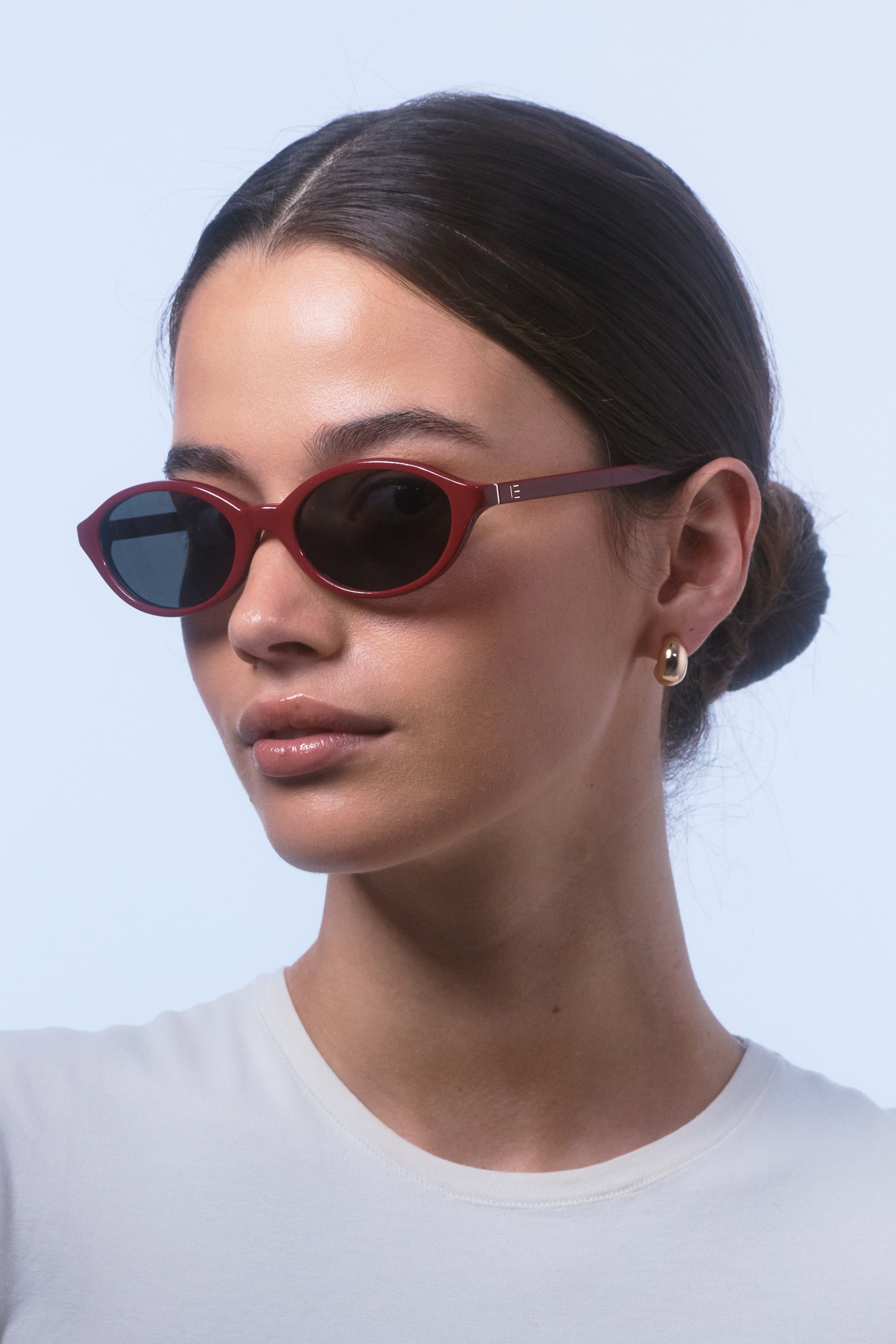 Female model wearing Isle of Eden Mirabel dark red sunglasses, angled portrait looking away