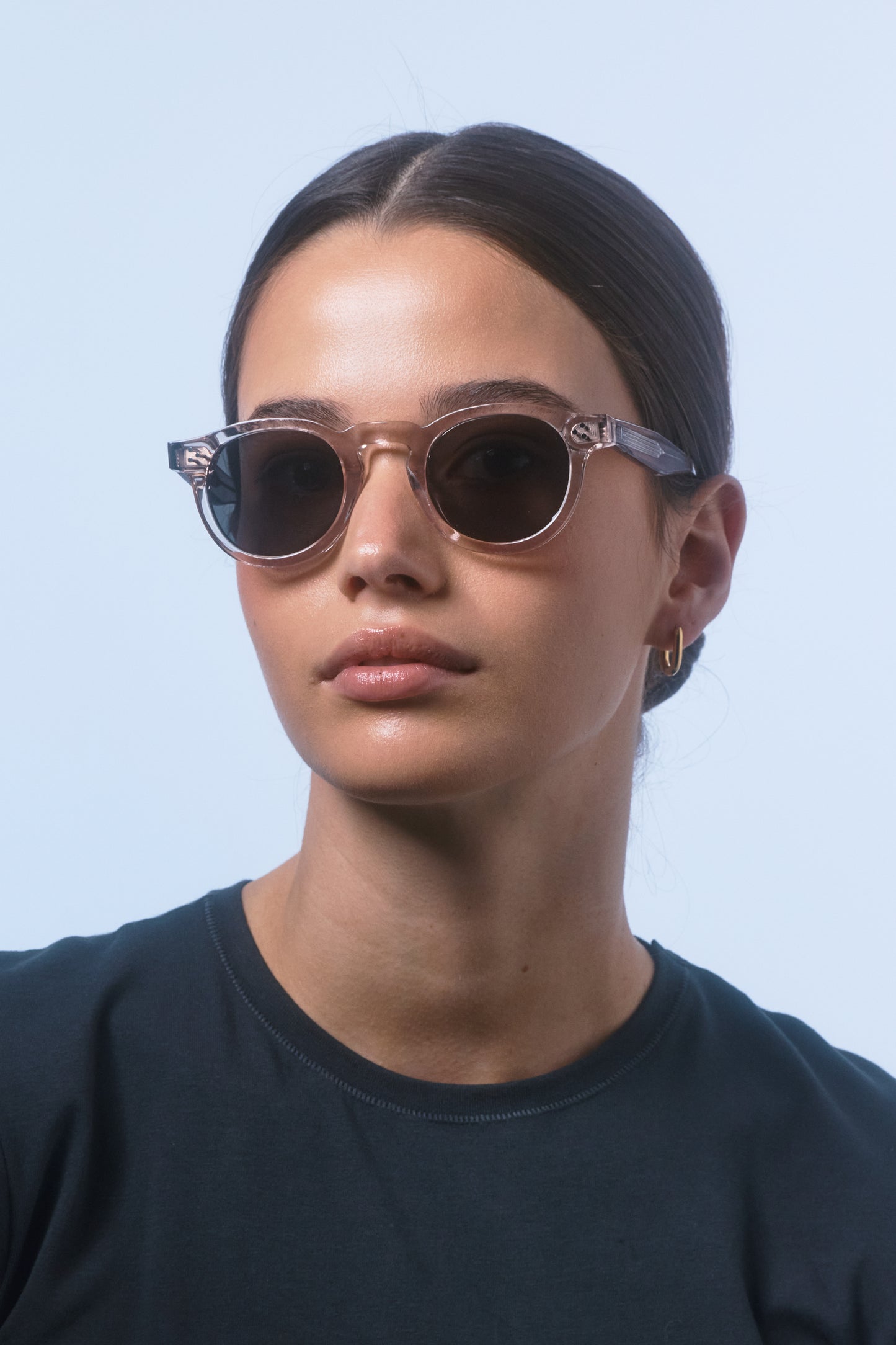Female model in a black shirt wearing Isle of Eden Drew sand Prescription round sunglasses, looking to the camera.