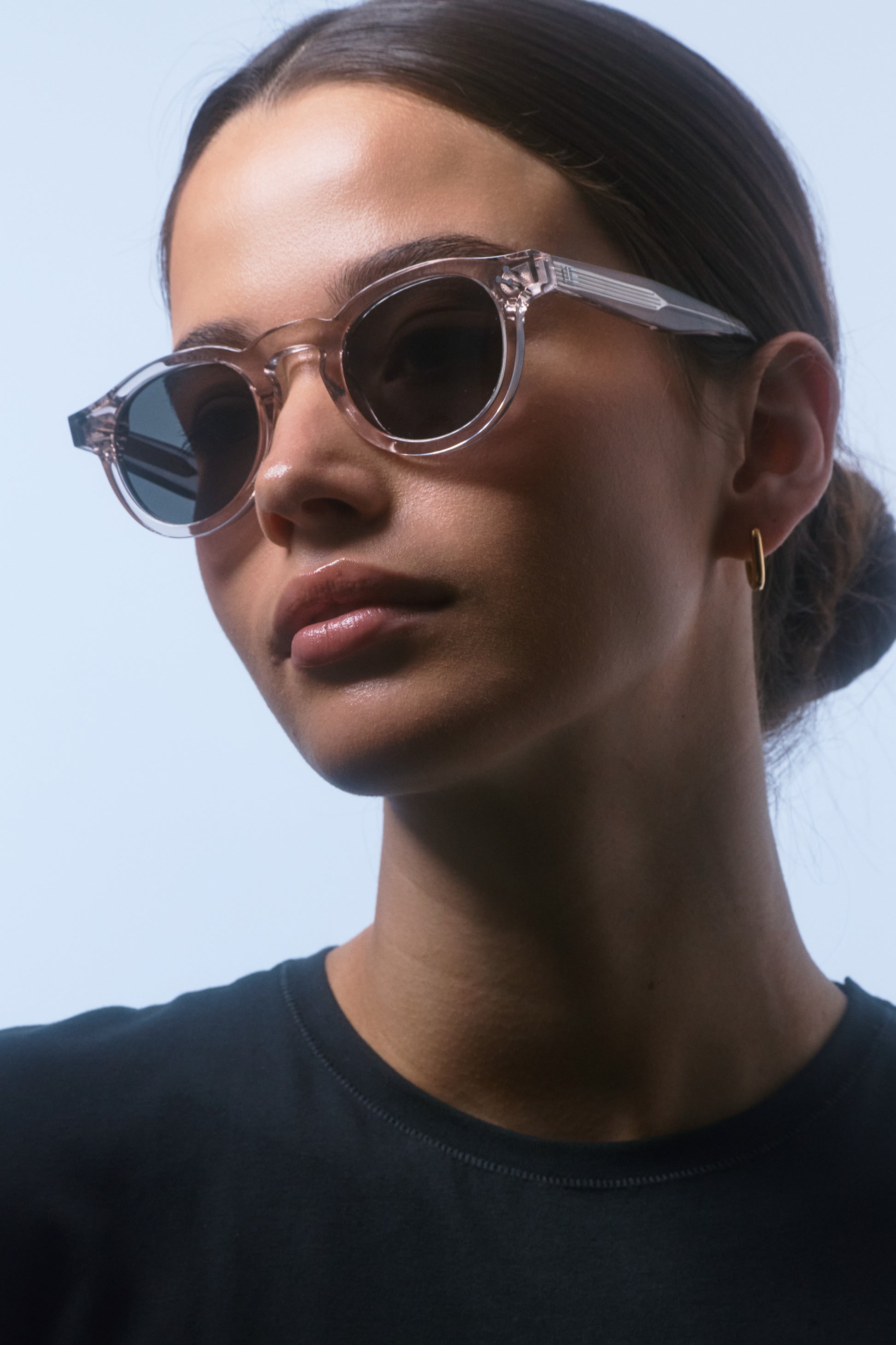 Female model in a black shirt, close-up wearing Isle of Eden Drew sand Prescription round sunglasses, looking to the side.