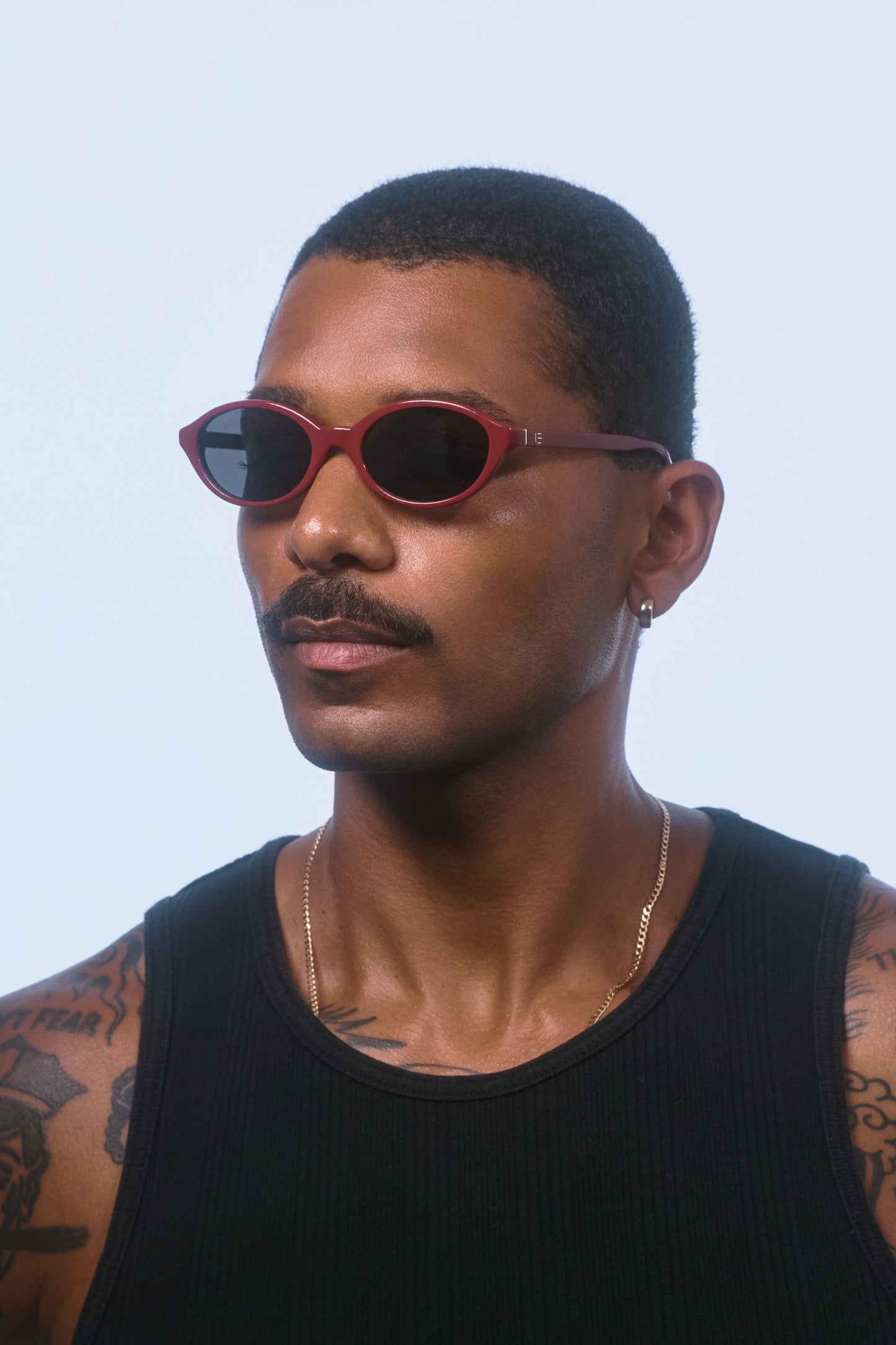 Male model wearing Isle of Eden Mirabel dark red sunglasses, angled portrait looking away