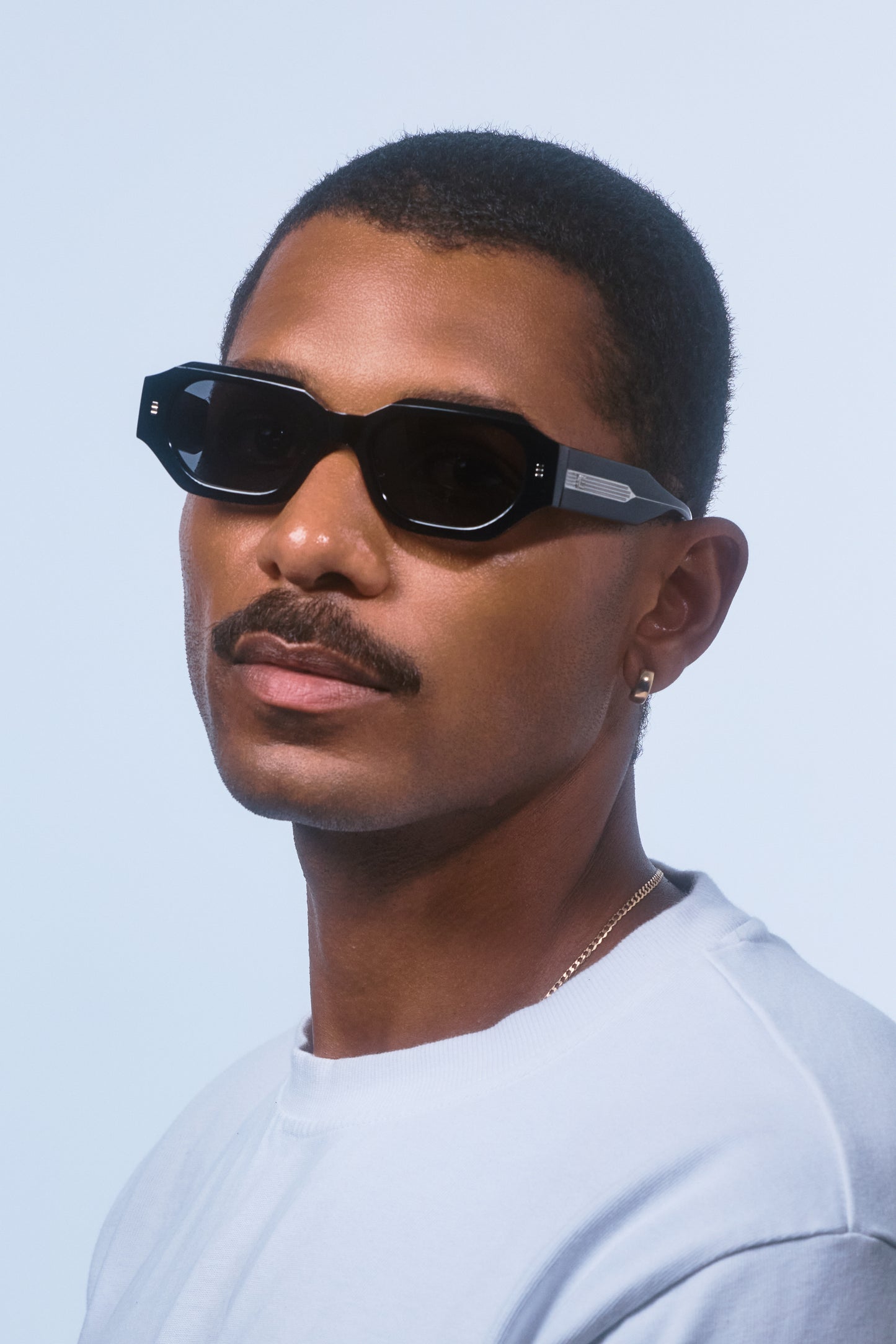 Man wearing Isle of Eden Blake Black Wire hexagonal sunglasses, angled portrait against a light blue background
