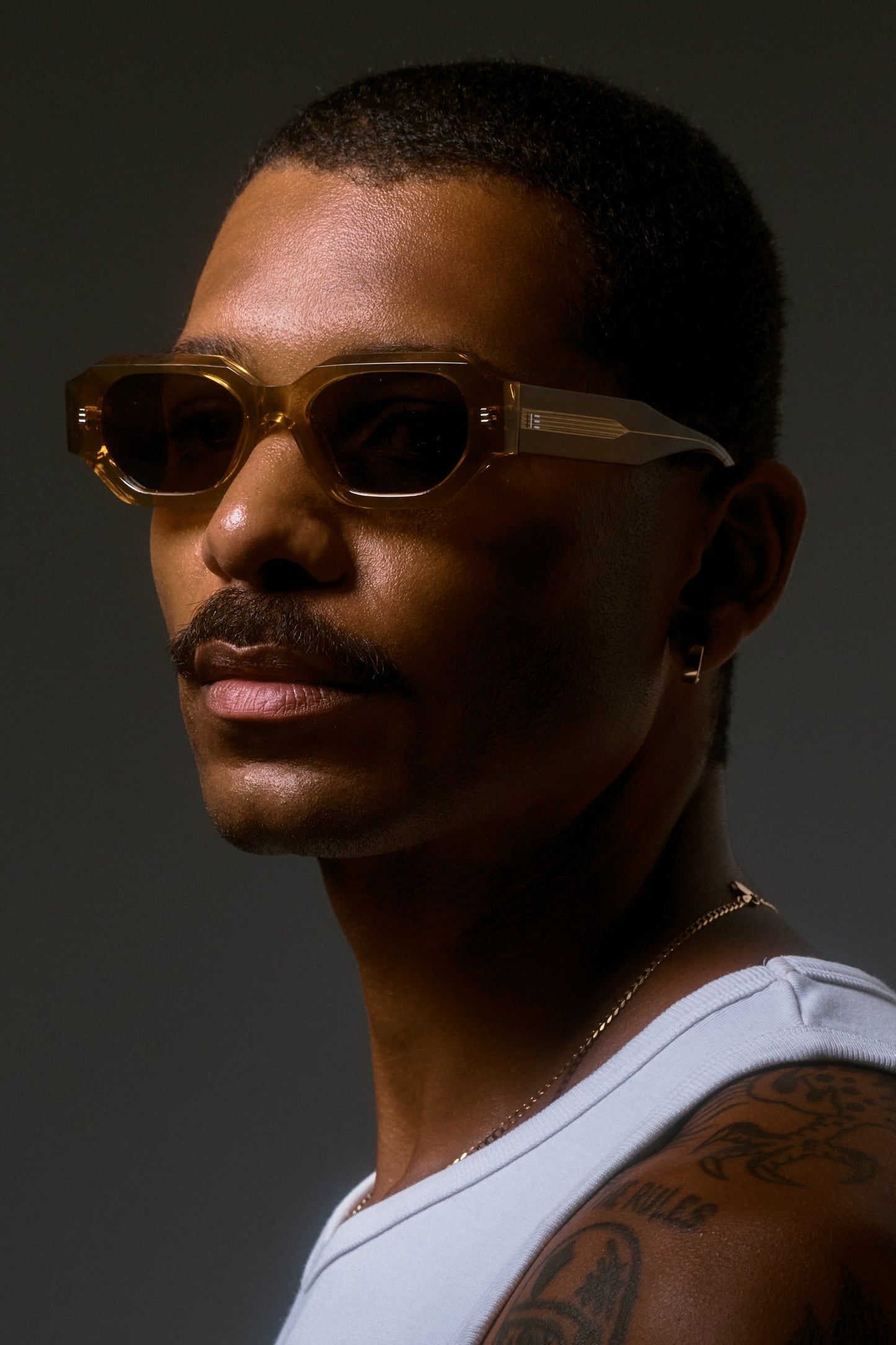 Male model wearing Isle of Eden Blake cognac sunglasses, angled side profile portrait with dramatic lighting