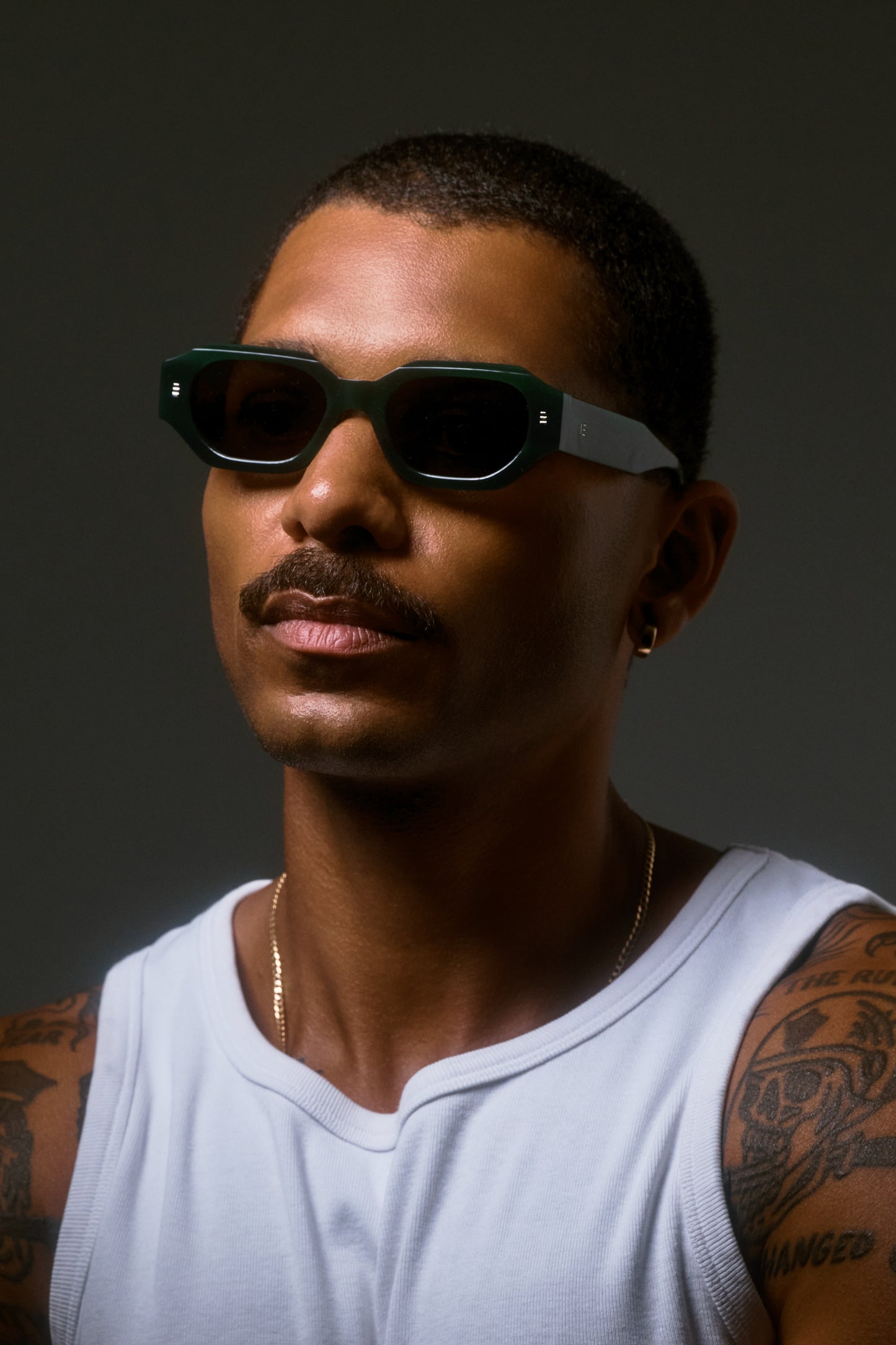 Male model wearing Isle of Eden Blake emerald sunglasses, angled side profile portrait with dramatic lighting