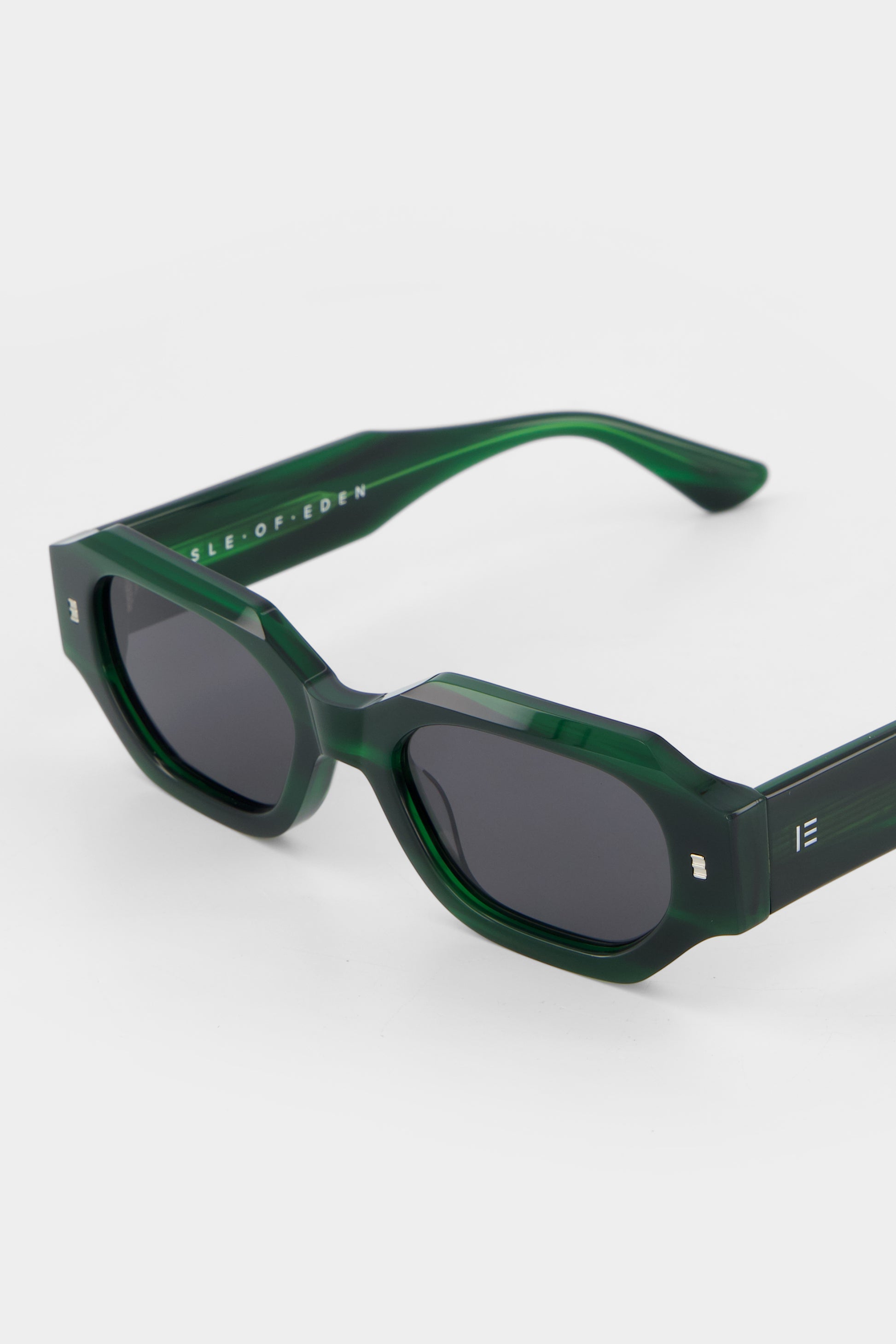 Close-up of Isle of Eden Blake emerald sunglasses showing filigree wire temple core and brand lettering