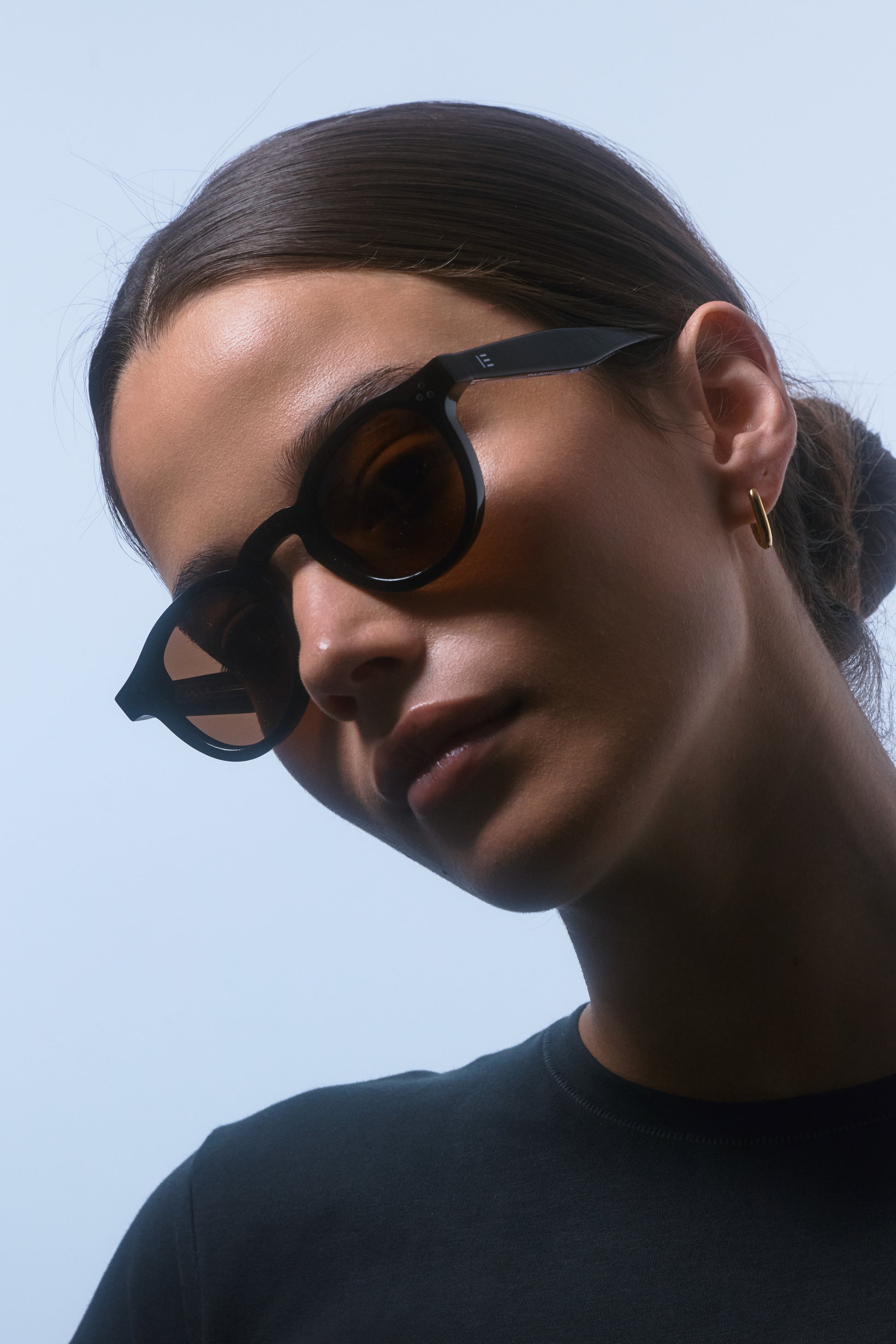 Female model in a black shirt wearing Isle of Eden Drew Black Prescription round sunglasses, looking to the side.