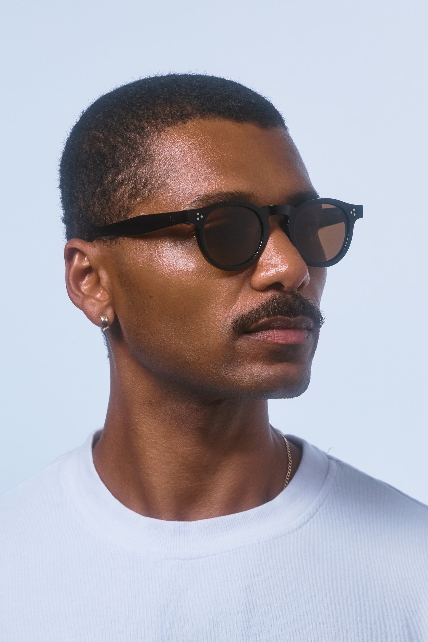 Male model in a white shirt wearing Isle of Eden Drew Black Prescription round sunglasses, looking to the side.