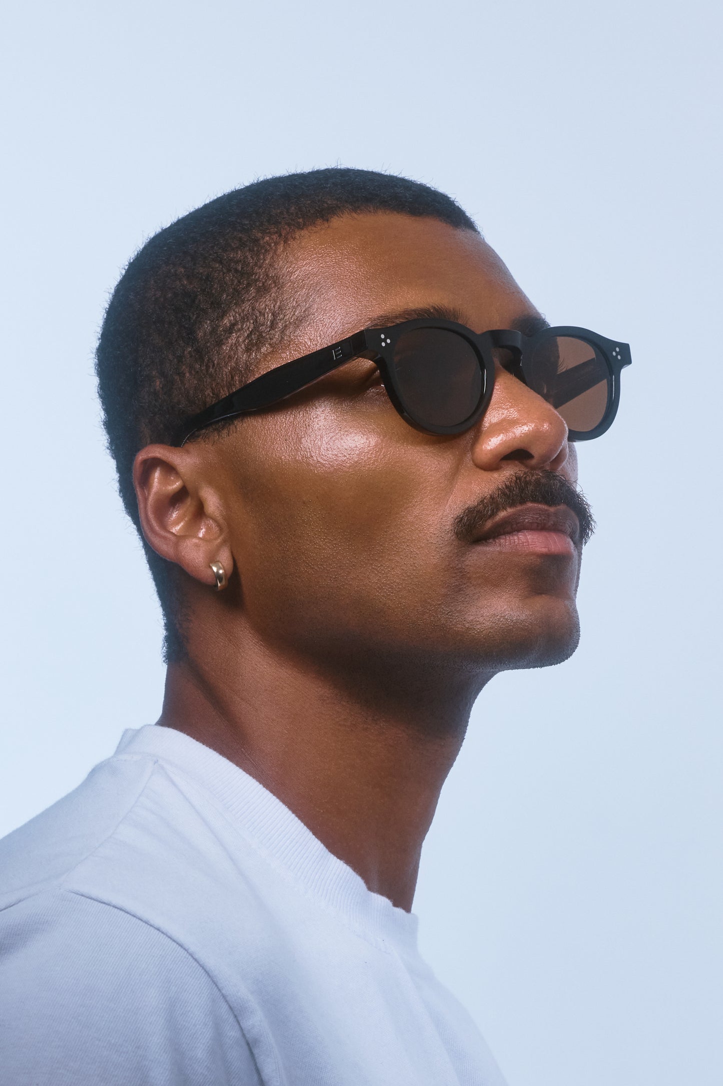 Male model wearing Isle of Eden Drew Black Prescription round sunglasses, looking up and away from camera.