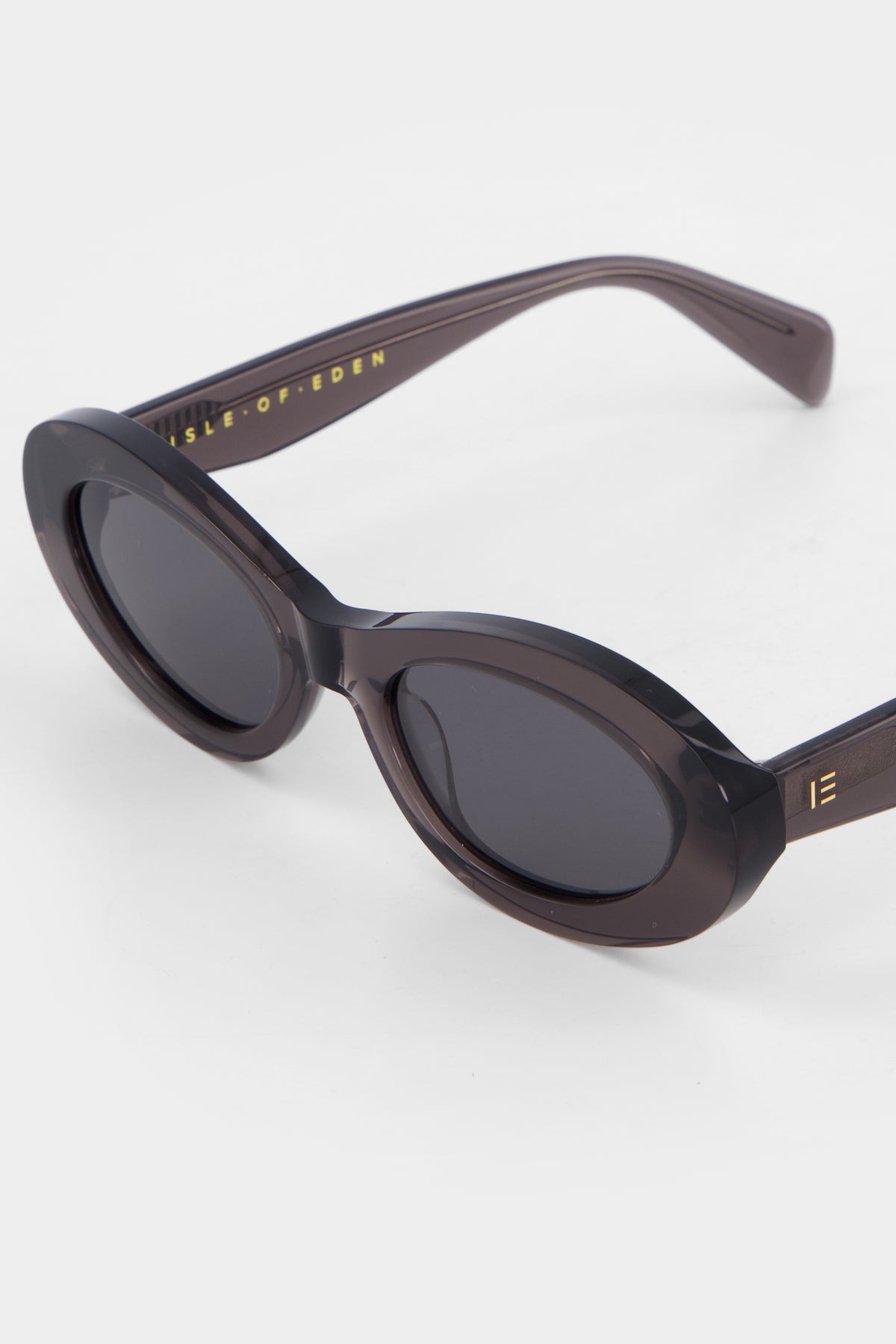 Close-up of Isle of Eden Frankie grey sunglasses showing curvy oval frame and brand lettering