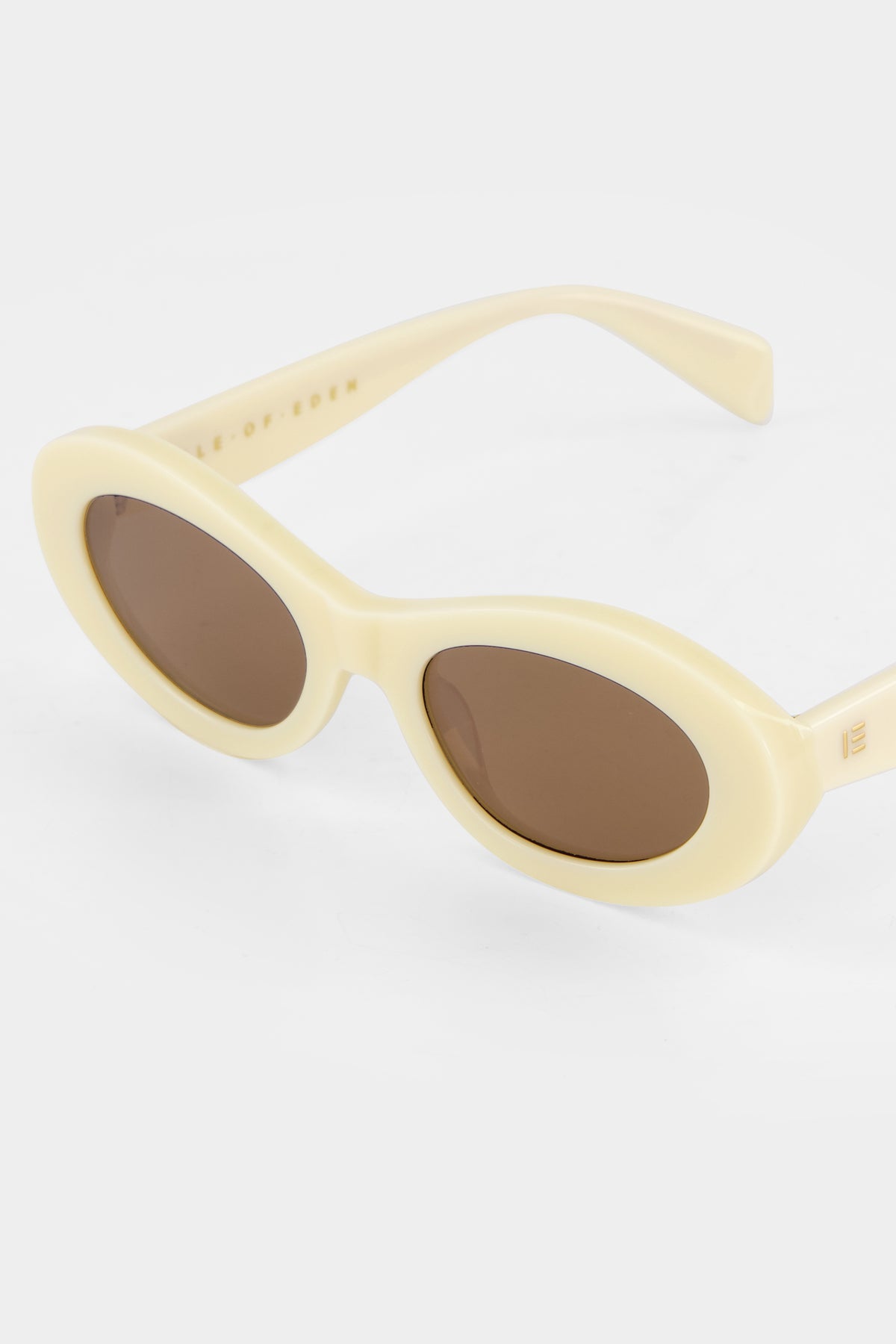 Close-up of Isle of Eden Frankie ivory sunglasses showing curvy oval frame and brand lettering