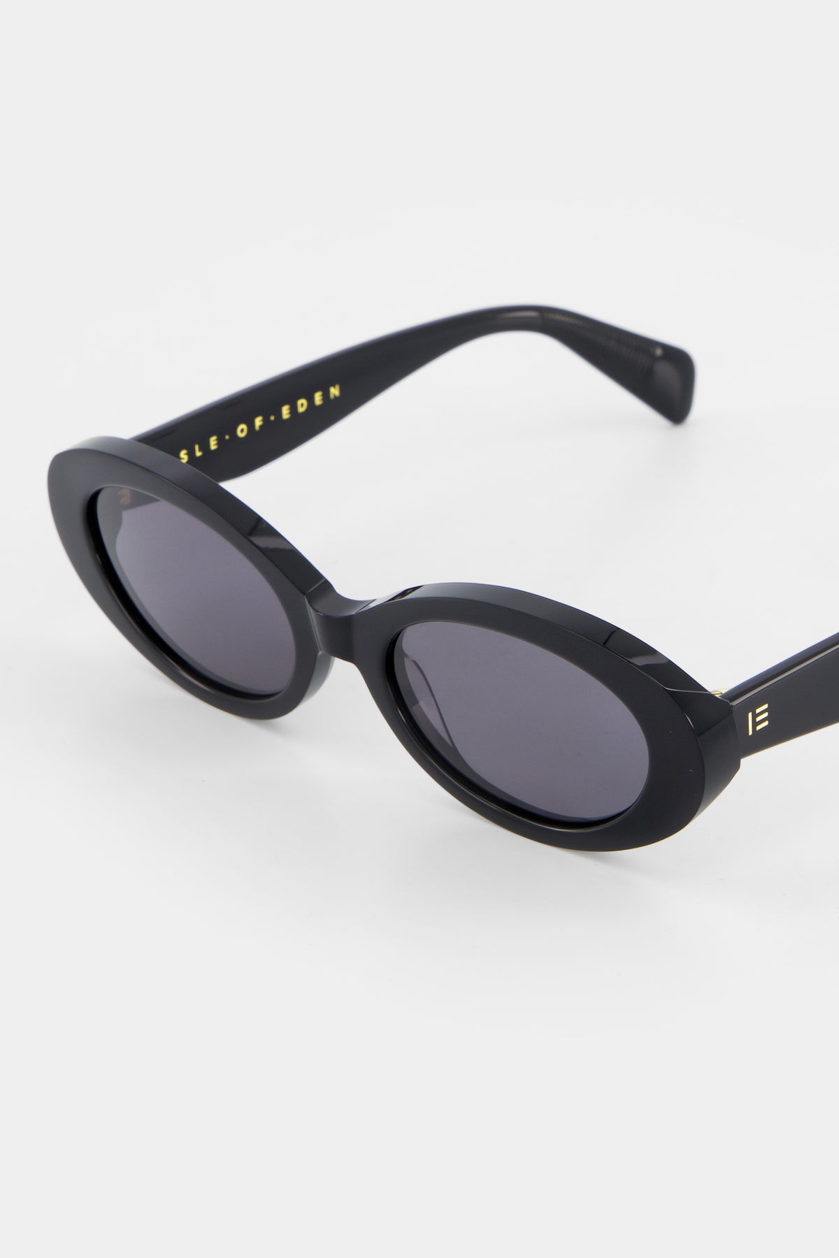 Close-up of Isle of Eden Frankie black sunglasses showing curvy oval frame and brand lettering