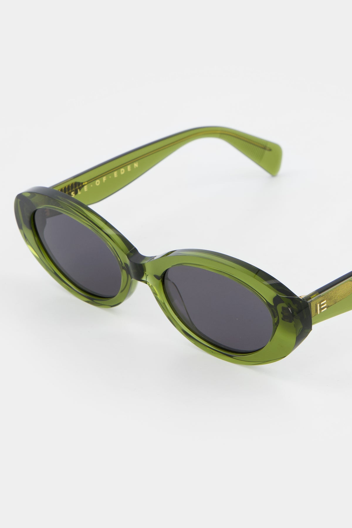 Close-up of Isle of Eden Frankie bottle green sunglasses showing curvy oval frame and brand lettering
