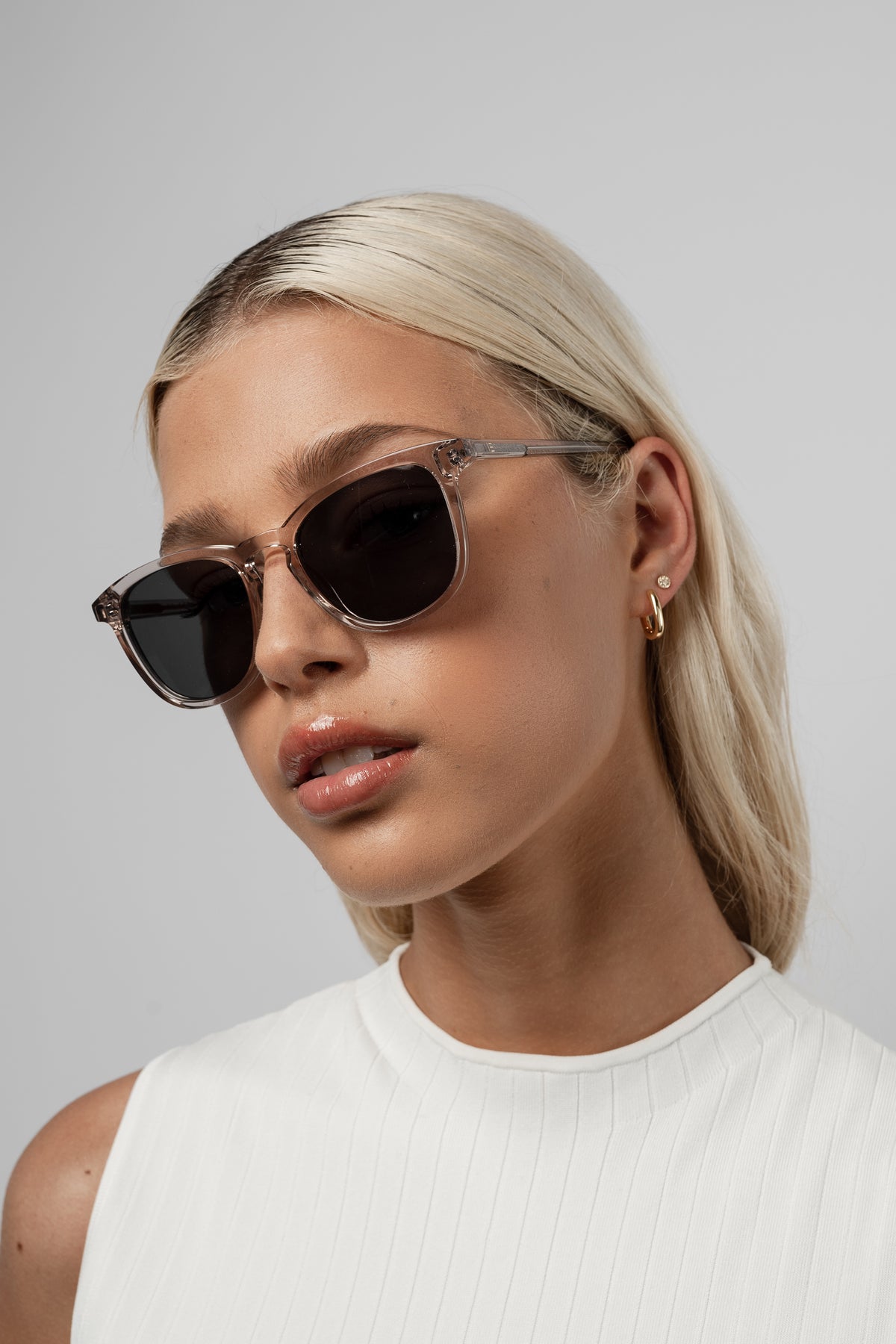 Woman wearing Isle of Eden Louis-Philippe sand sunglasses, chin lowered, looking at camera against a white background