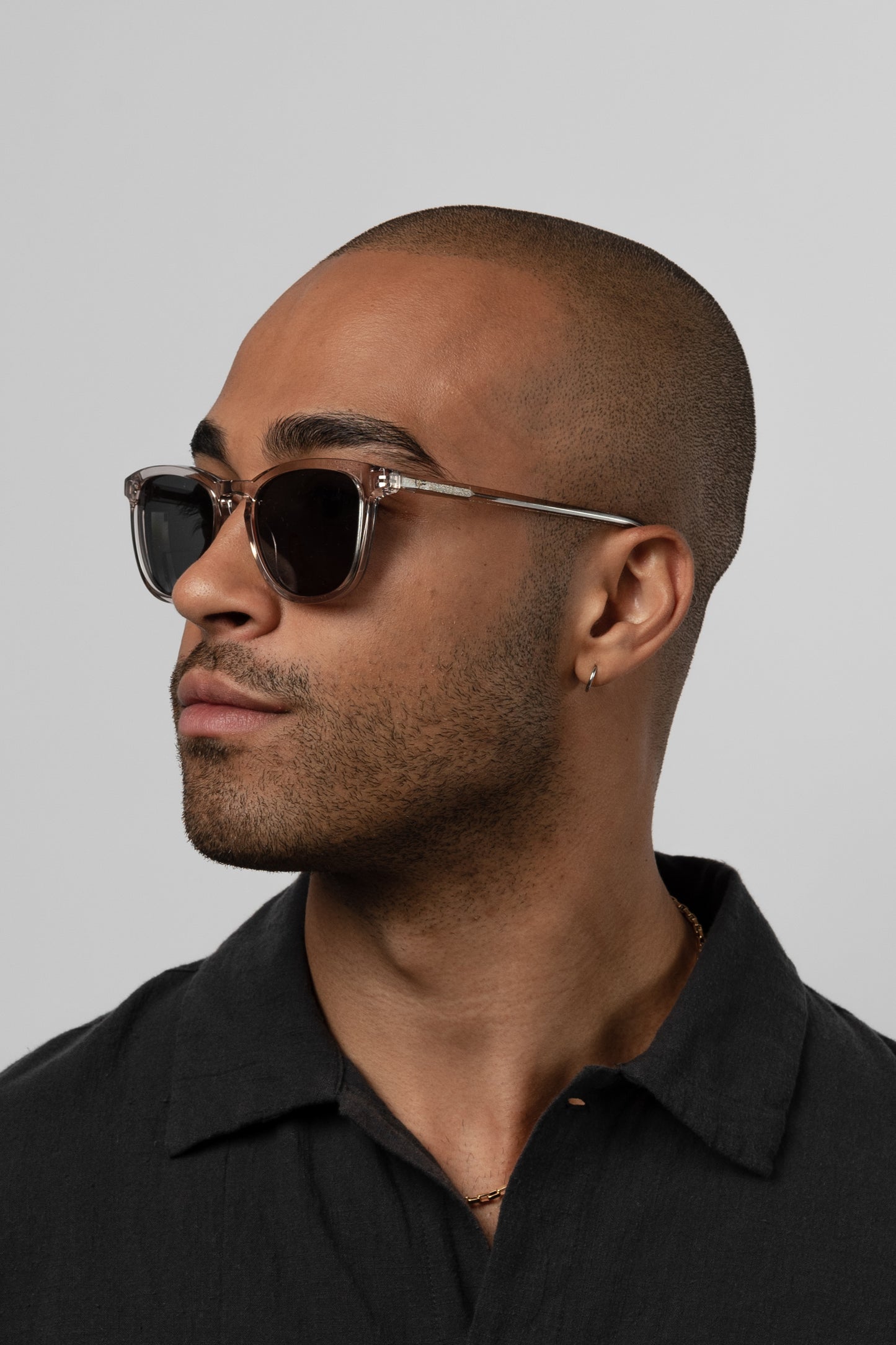 Man wearing Isle of Eden Louis-Philippe sand sunglasses, angled side profile against a grey background