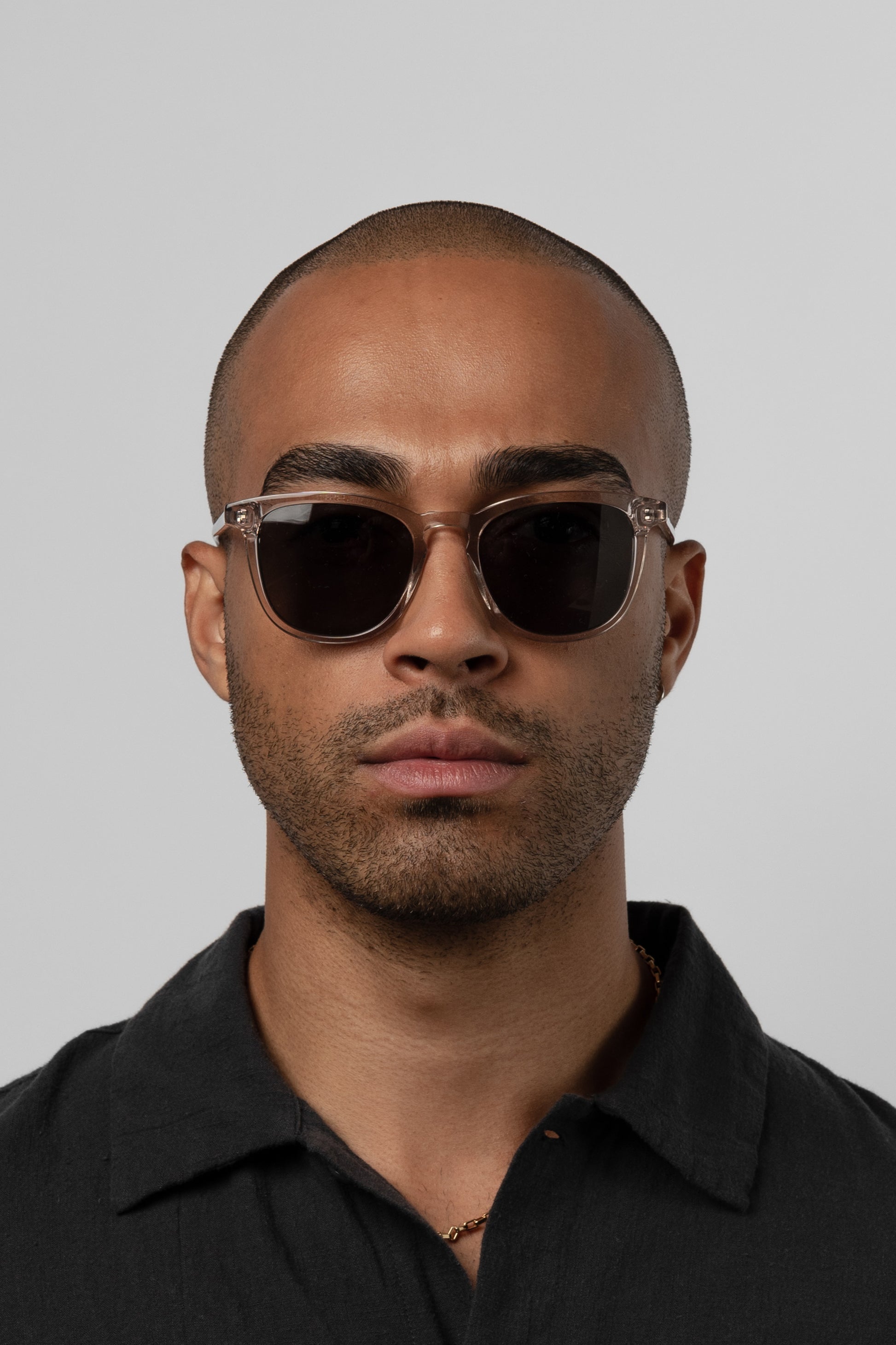 Man wearing Isle of Eden Louis-Philippe sand sunglasses, front-facing portrait against a grey background