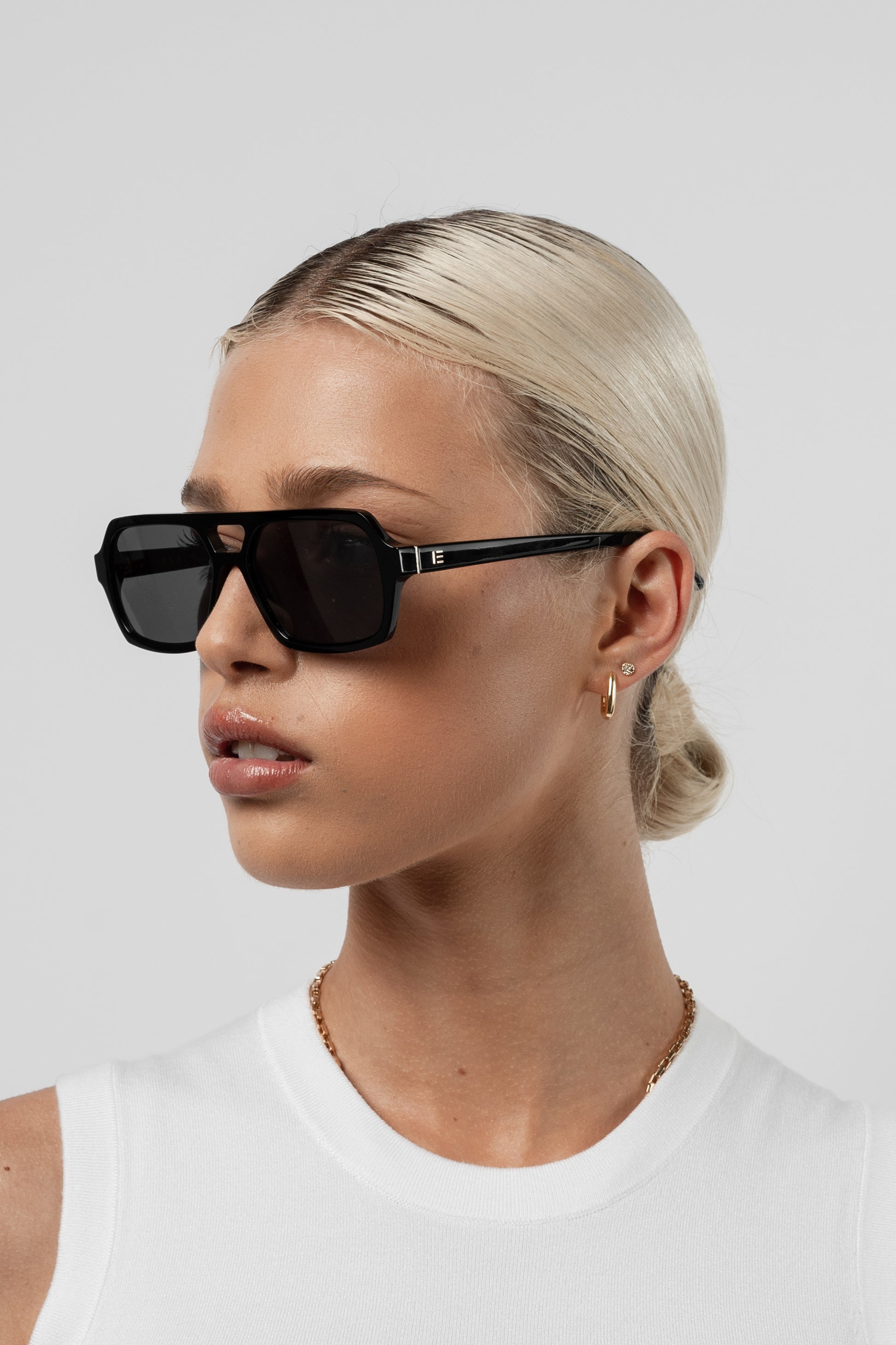 Female model wearing Isle of Eden Lola black sunglasses, angled portrait looking away