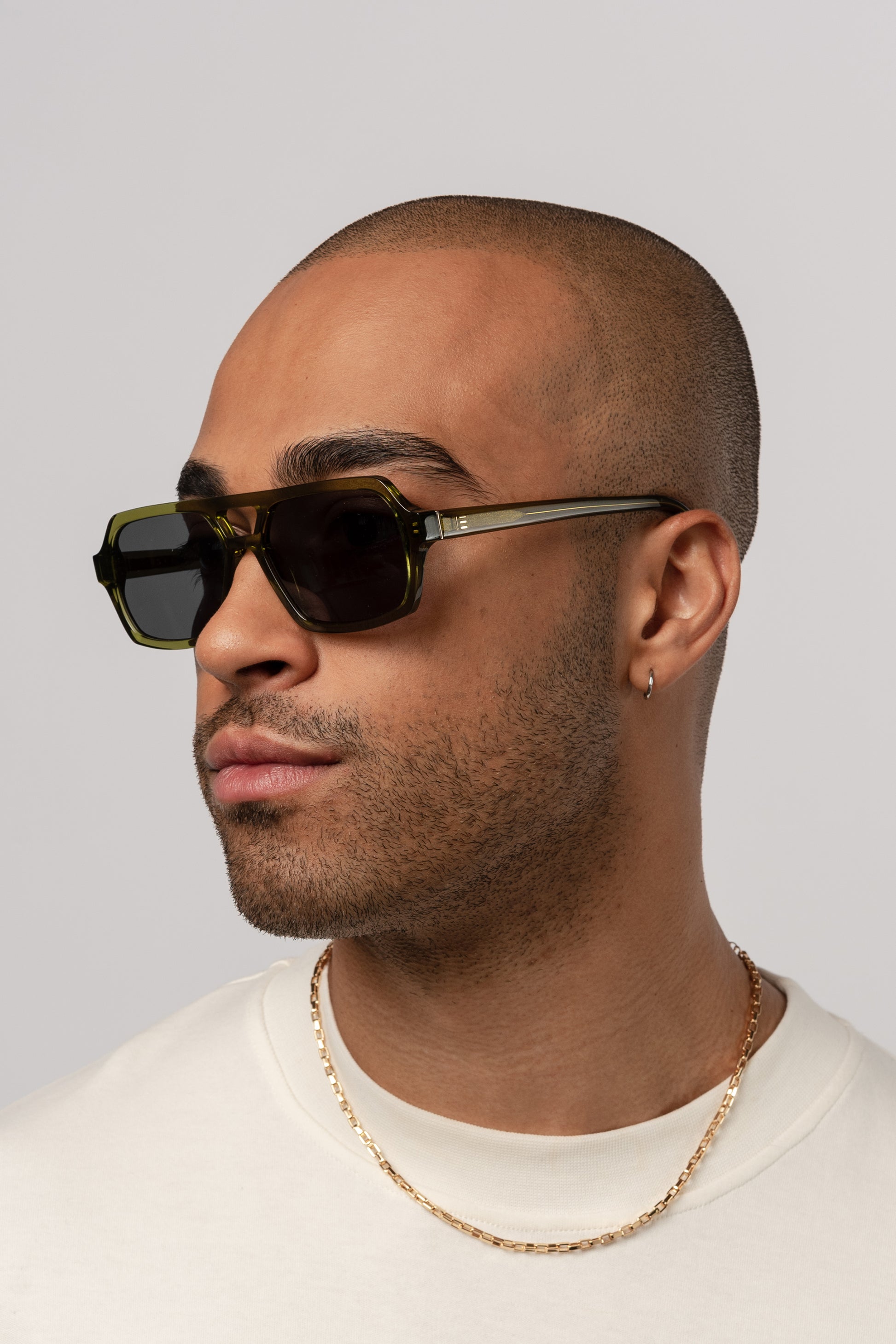 Male model wearing Isle of Eden Lola bottle green sunglasses, angled portrait looking away