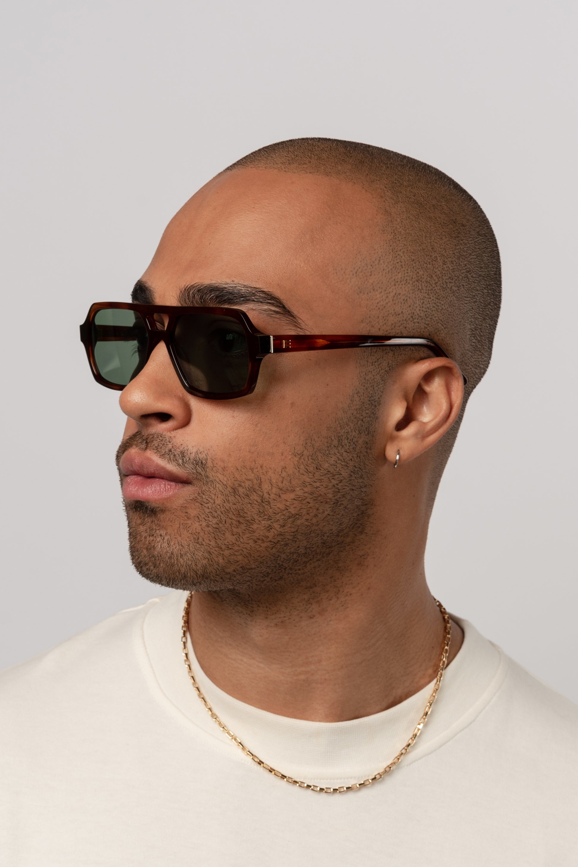 Male model wearing Isle of Eden Lola honey tortoise sunglasses, angled portrait looking away
