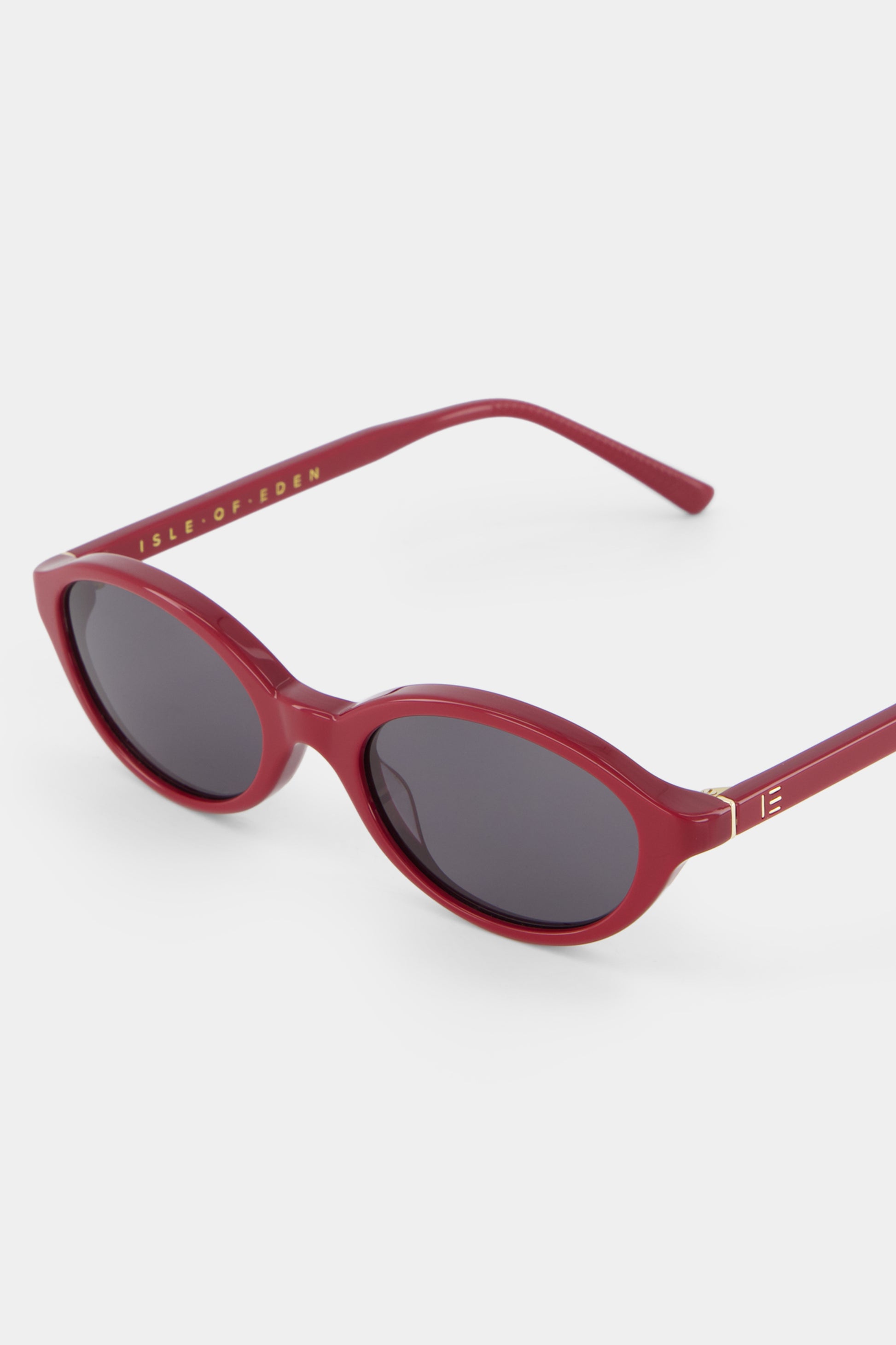 Close-up of Isle of Eden Mirabel dark red sunglasses showing sleek oval frame and brand lettering