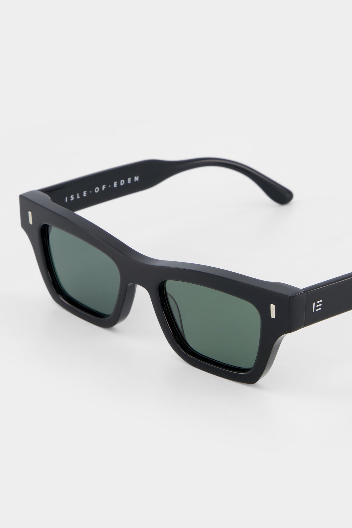 Close-up of Isle of Eden Olli black sunglasses showing low-profile art-deco frame and brand lettering