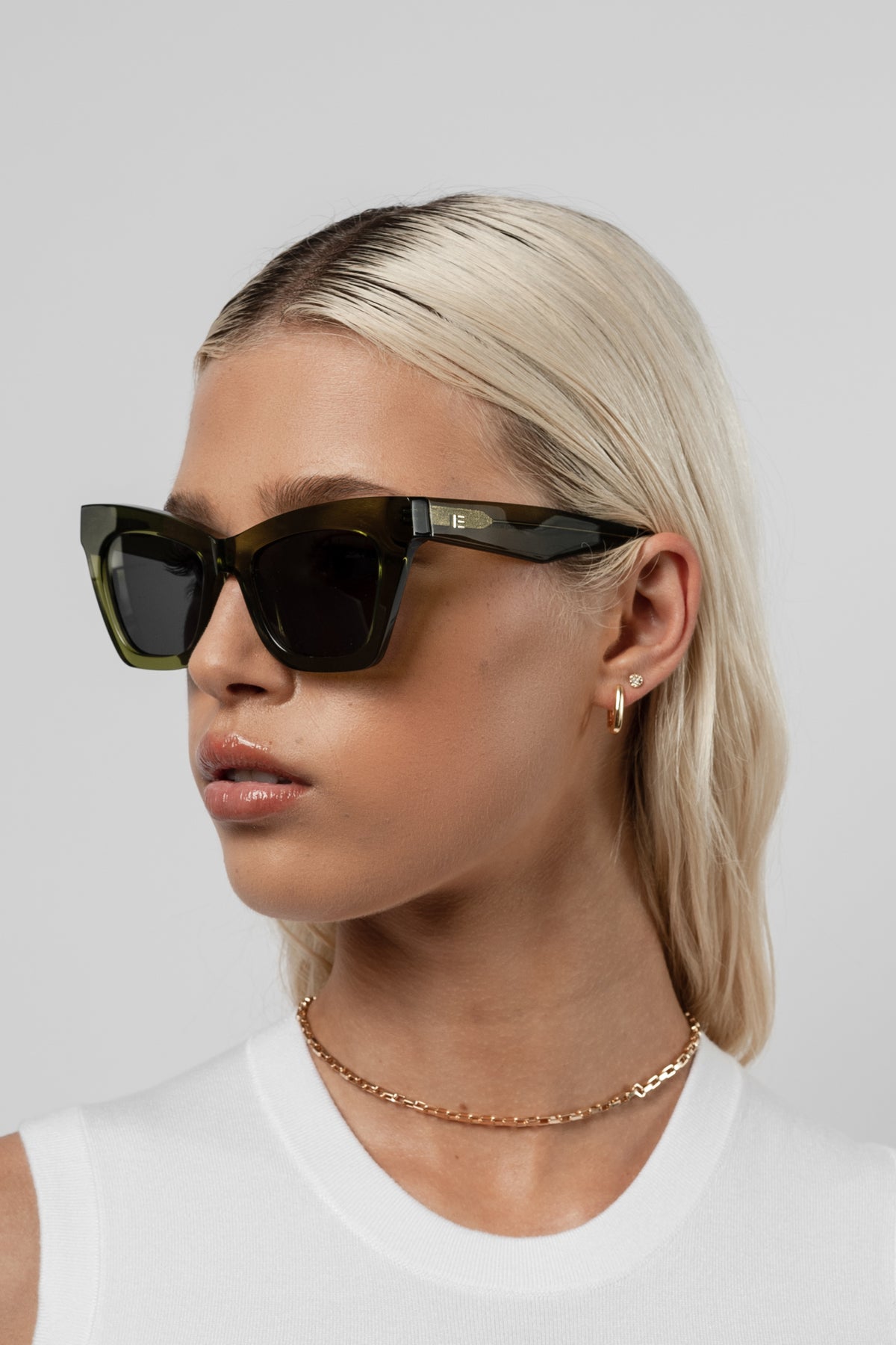 Woman wearing Isle of Eden Sienna bottle green sunglasses, angled portrait against a light background